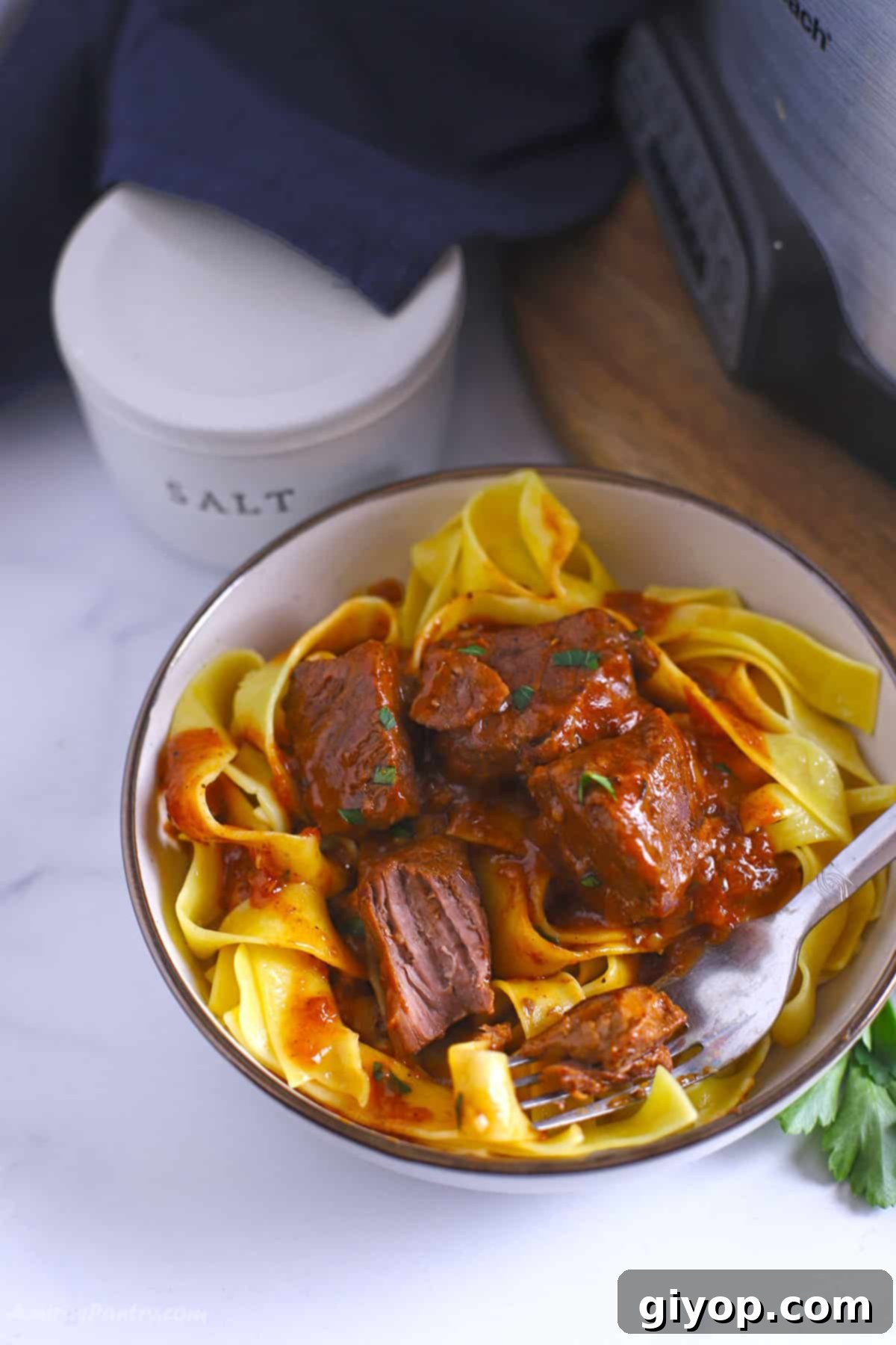 A close up image of a bowl with beef and noodles, showcasing tender meat and rich sauce over noodles.