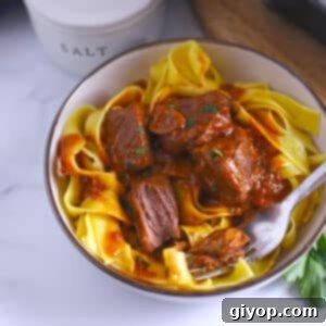 A white bowl with beef cubes on egg noodles.