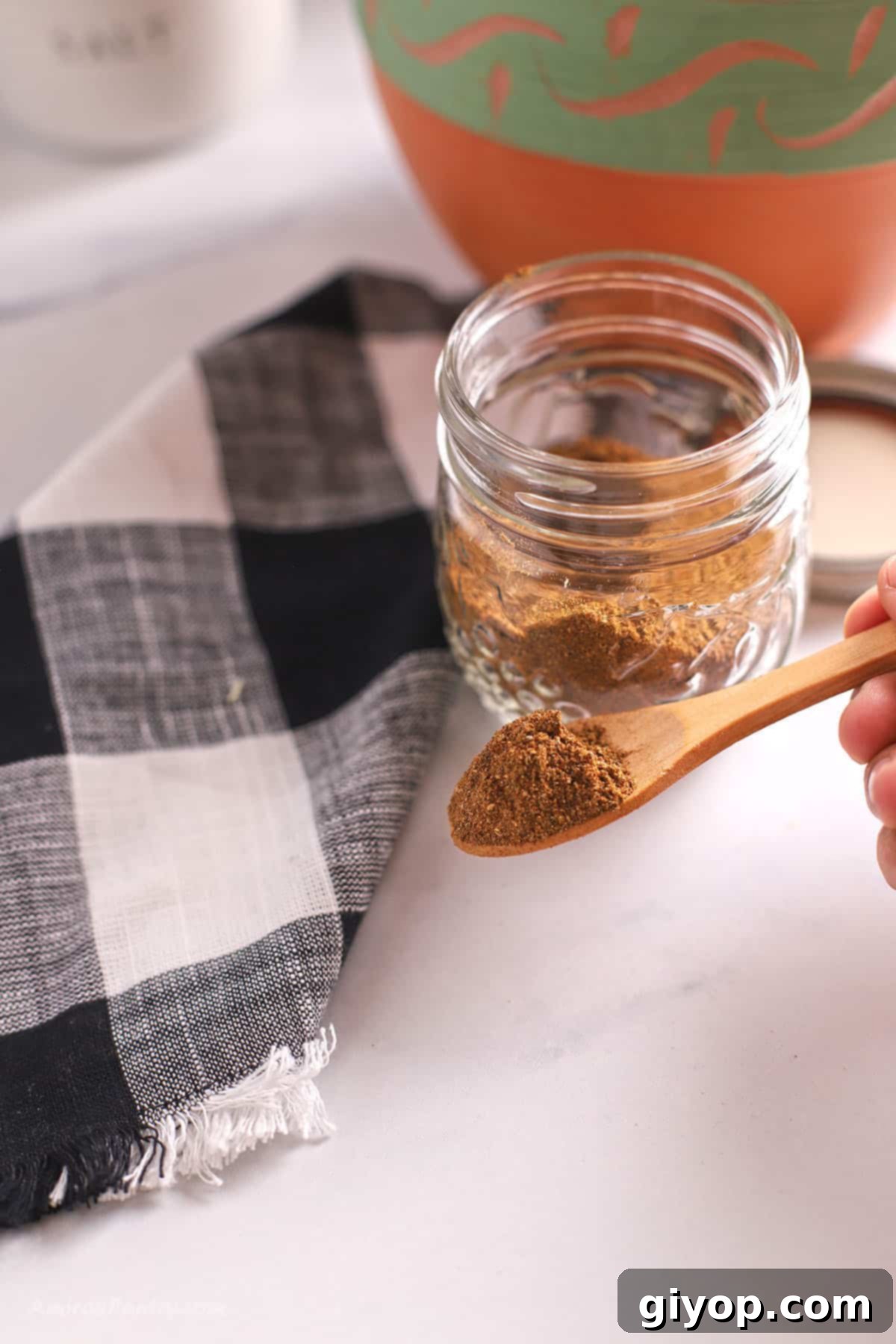 Scooping some shawarma seasoning with a wooden spoon from a glass spice jar.