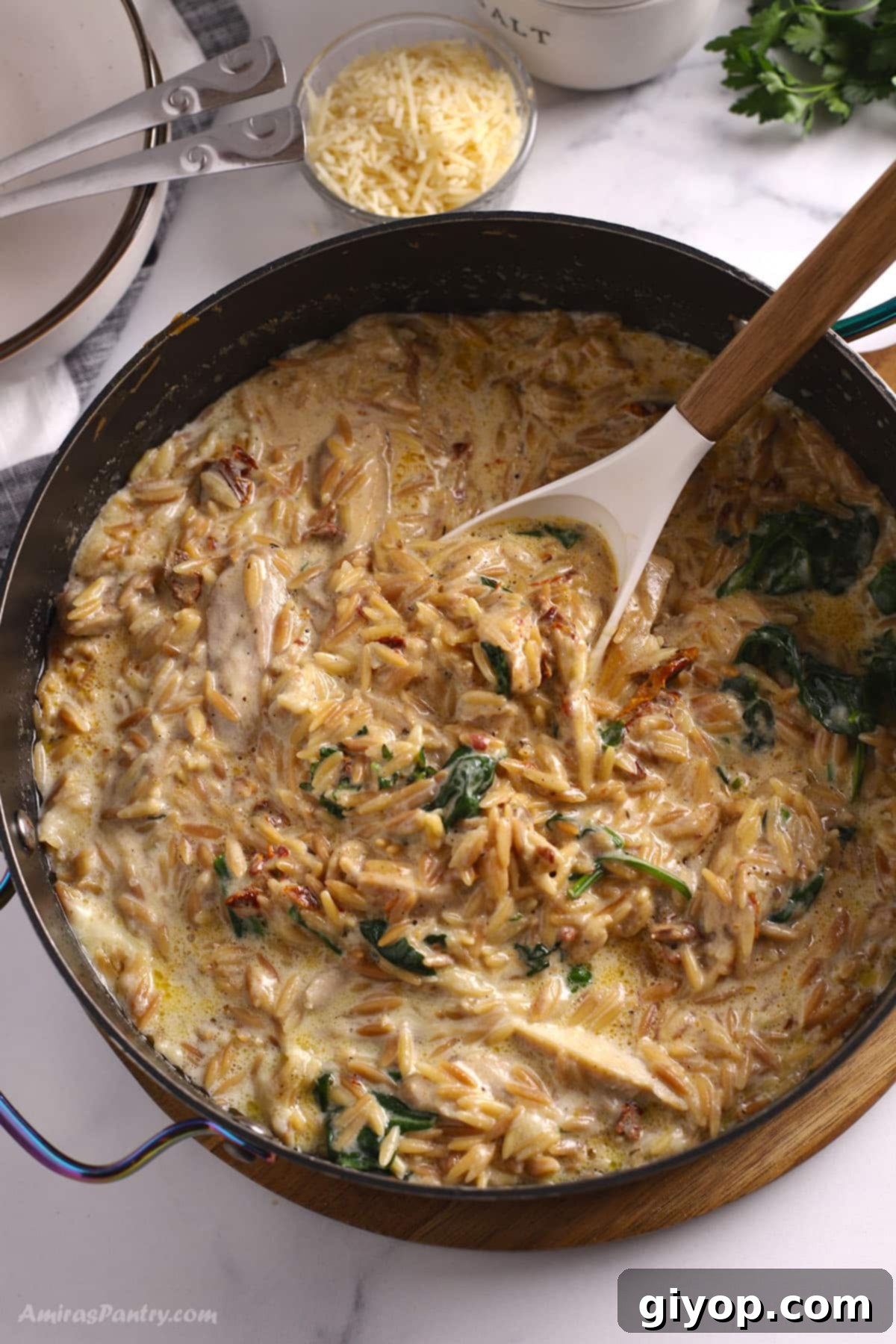 An overhead image of a large skillet with creamy Tuscan Chicken Orzo, garnished with fresh herbs.