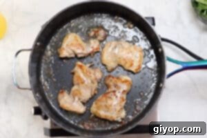 Chicken thighs searing in a hot skillet until golden brown.
