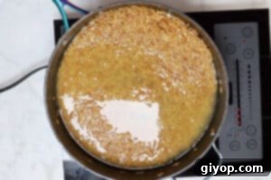 Orzo cooking in chicken broth, covered, in a non-stick skillet.