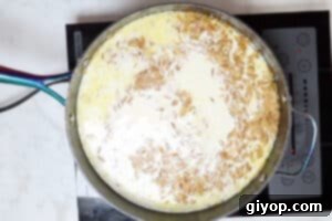 Milk and heavy cream being poured into the skillet with cooked orzo.