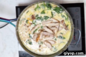 Sliced cooked chicken being added back into the creamy Tuscan orzo in the skillet.