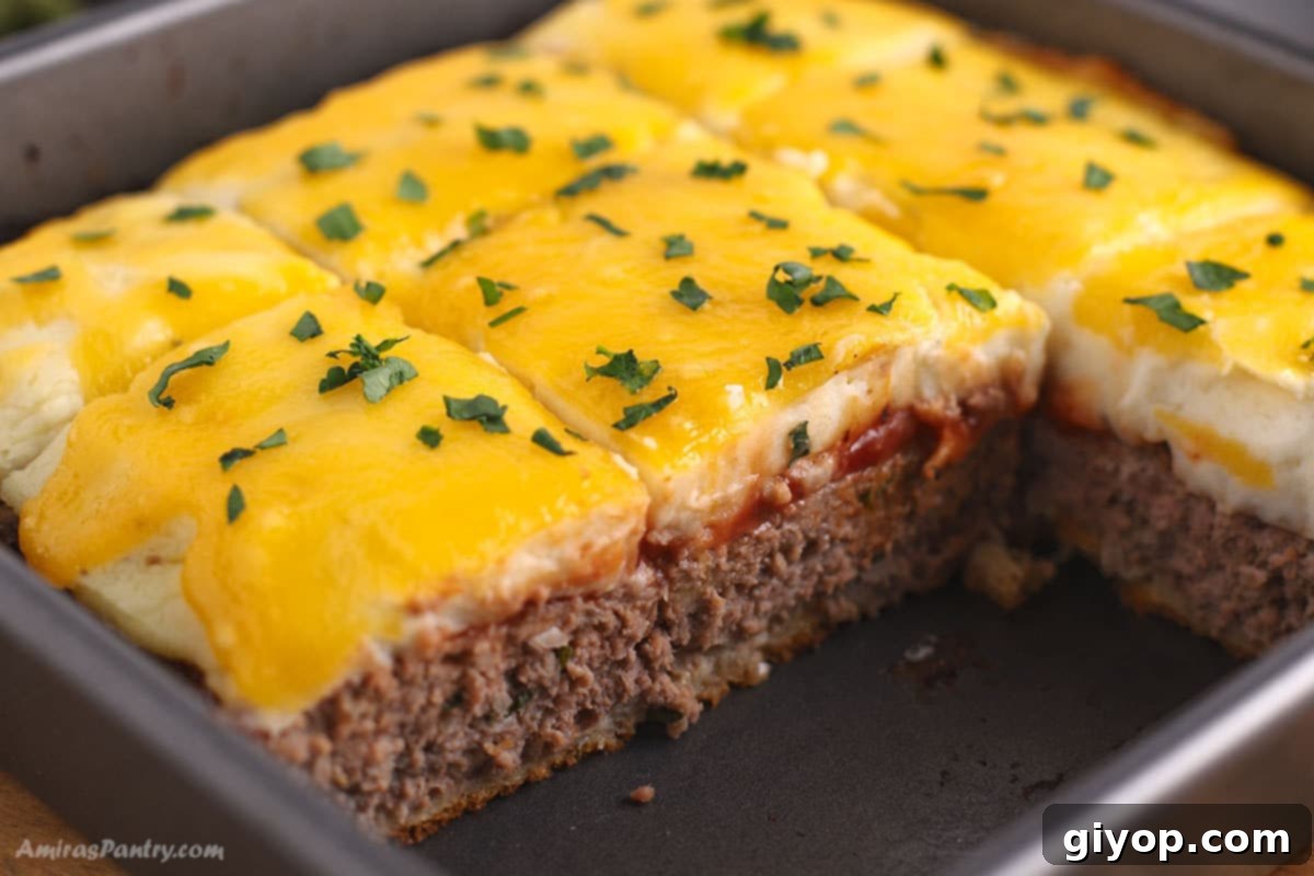 A close-up image of a Meatloaf Casserole cut to show its distinct layers of savory meatloaf, creamy mashed potatoes, and melted cheese, ready to be served.