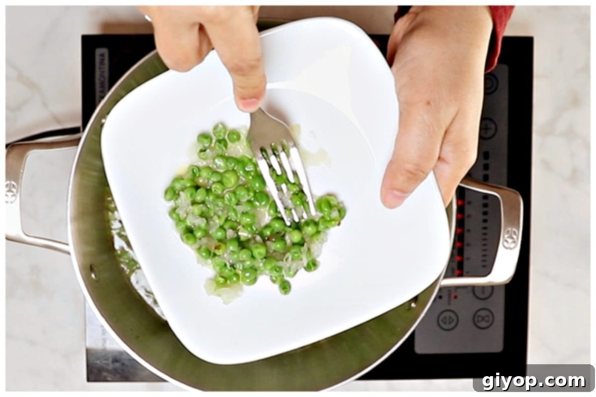 Creamy Pasta with Peas 6 Close-up of frozen peas being mashed with a fork on a small plate, creating a creamy texture for the pasta sauce.