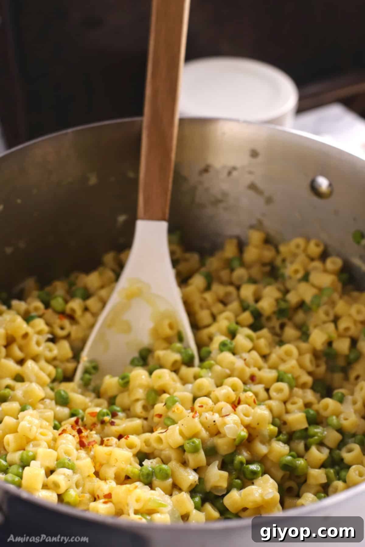 Creamy Pasta with Peas 9 Freshly cooked Pasta e Piselli in a stainless steel pot, garnished with a sprinkle of red pepper flakes, ready to be served or stored.