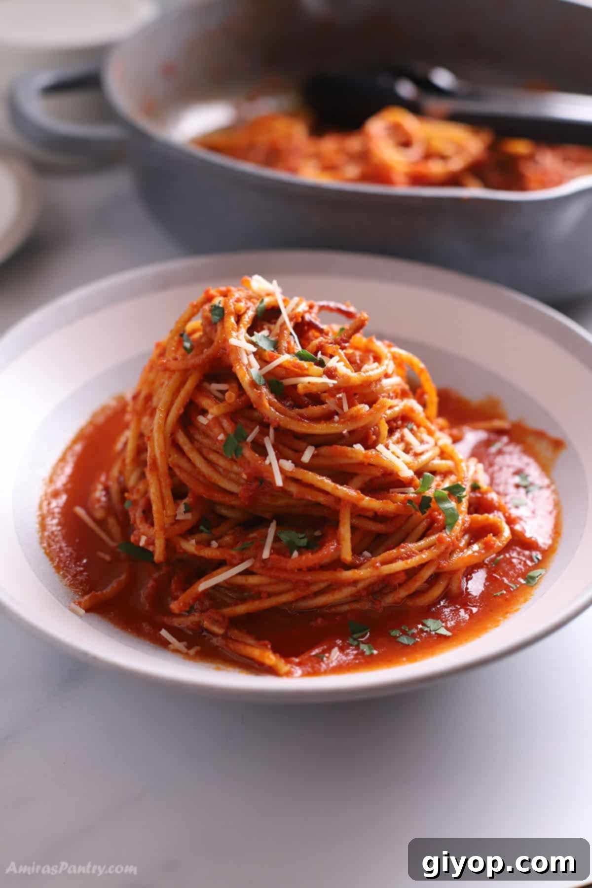 A large bowl filled with Spaghetti all'Assassina, showcasing its rich red color and charred noodles, with a cooking pot blurred in the background.