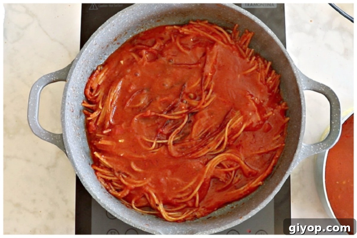 More rich tomato sauce being poured over the partially cooked and charred spaghetti in the pan.
