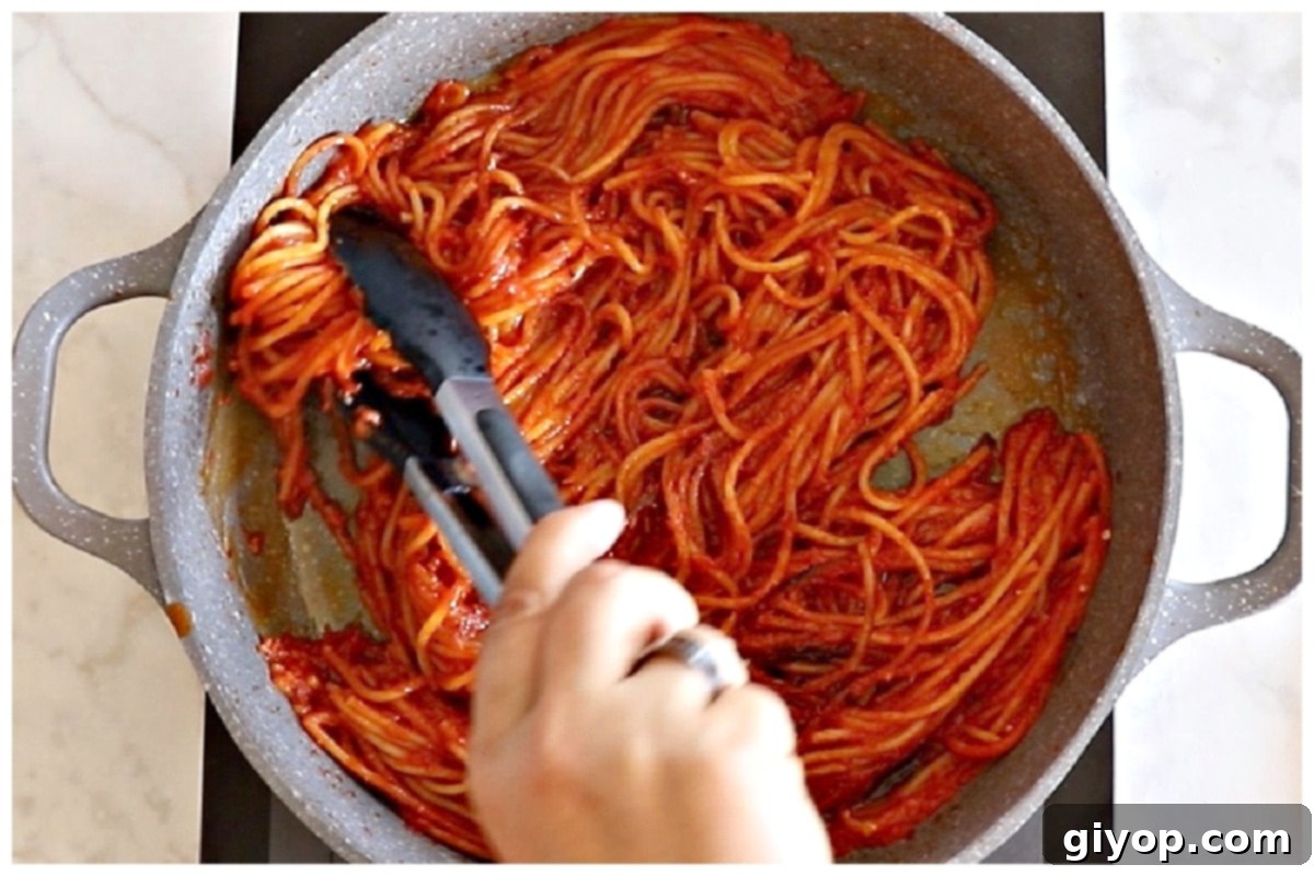 Using kitchen tongs to turn and mix spaghetti in a hot skillet for additional browning.
