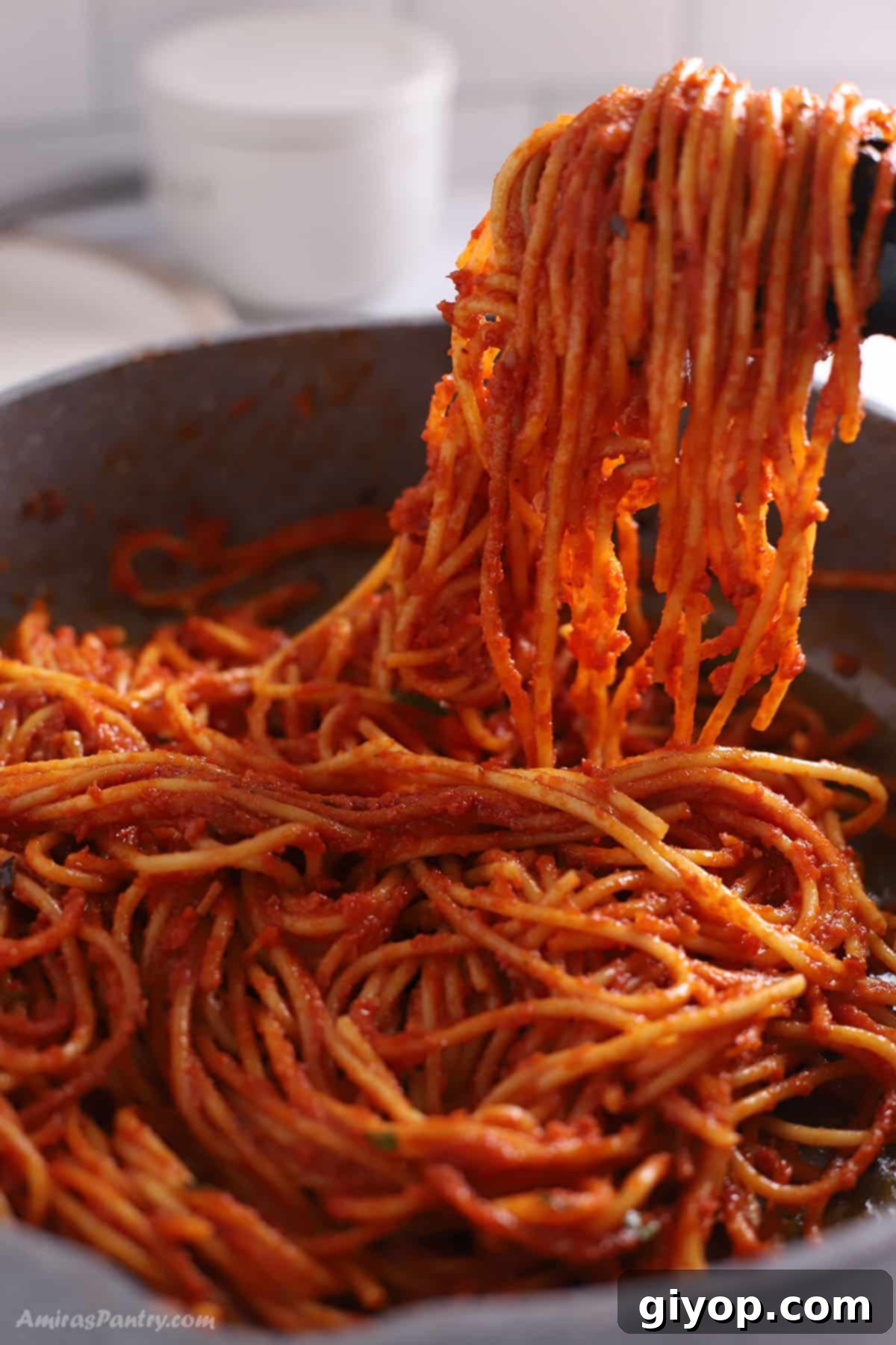 Kitchen tongs holding a portion of Spaghetti all'Assassina above a large skillet, showing the pasta's texture and rich sauce.