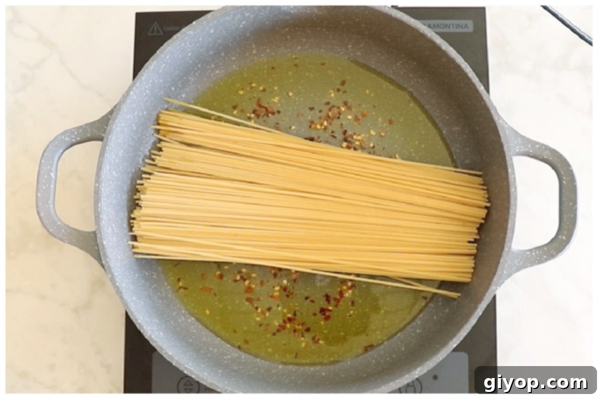 Dry spaghetti noodles being placed into a large skillet with chili-infused oil.