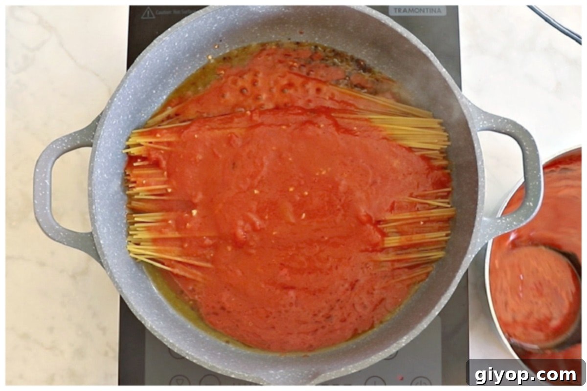 Rich tomato sauce being poured over spaghetti noodles in a large skillet.