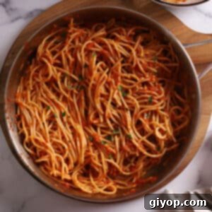 An overhead view of a large skillet filled with vibrant harissa pasta, garnished with fresh herbs.