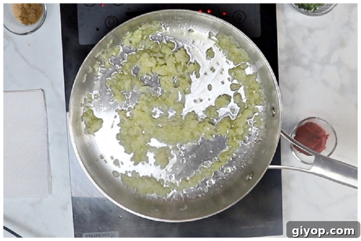 Sautéed onion and garlic gently sizzling in olive oil in a large skillet, forming the aromatic base for the harissa pasta sauce.