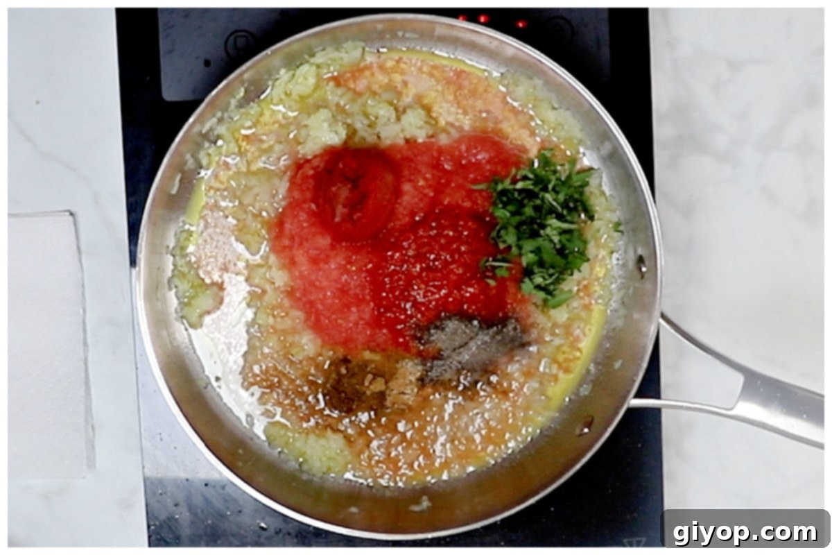 A skillet containing the vibrant red harissa pasta sauce ingredients, including tomatoes, harissa, and spices, simmering gently.