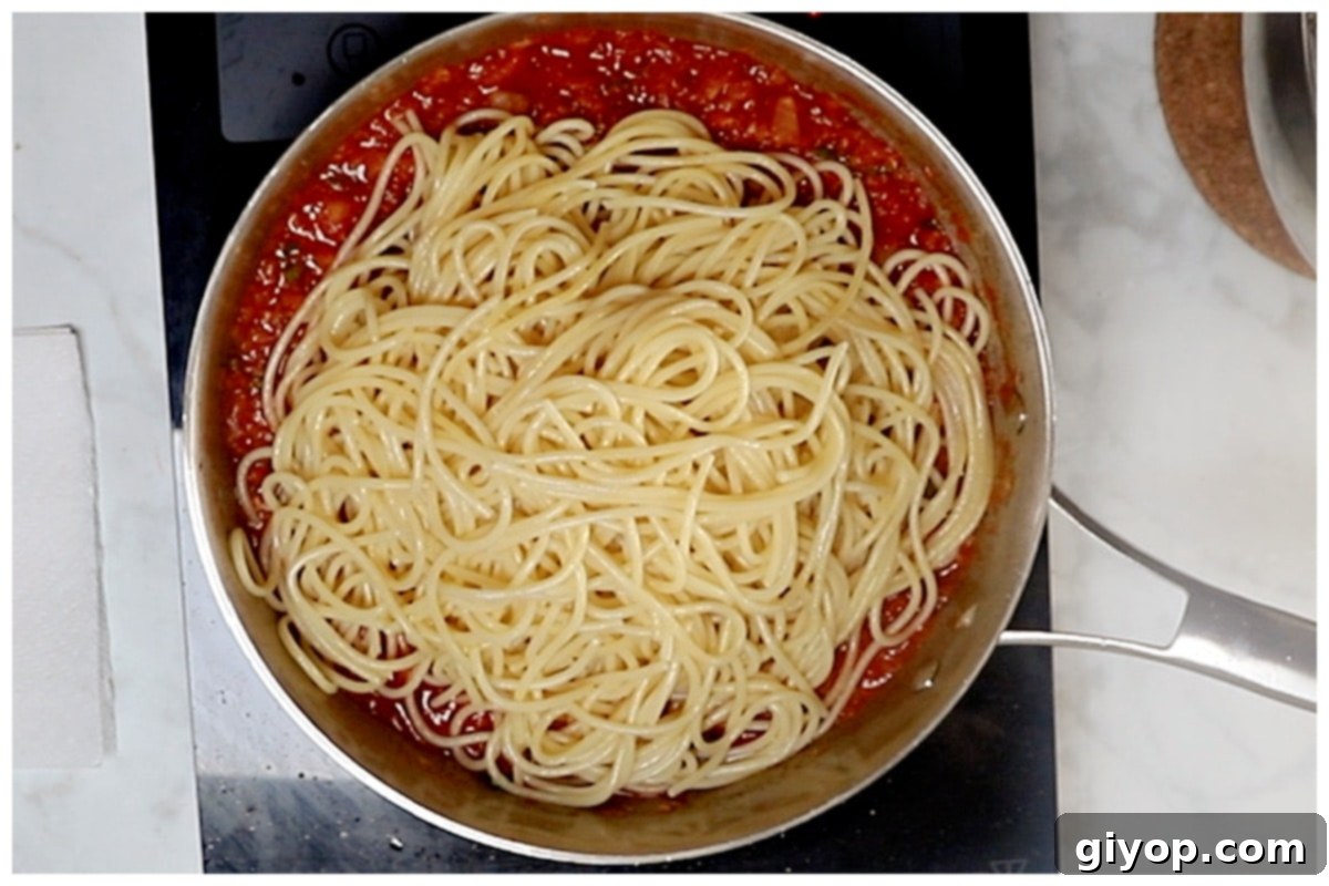 Al dente pasta being added to the skillet, ready to be tossed with the vibrant harissa tomato sauce.