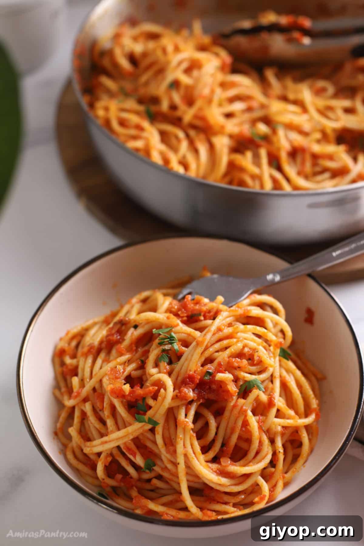 A small bowl of harissa pasta garnished with fresh coriander, with a large skillet of more pasta blurred in the background.