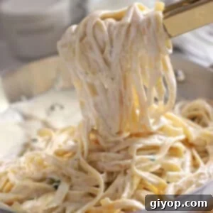 Kitchen tongs serving Alfredo pasta, showing the creamy coating of the sauce.
