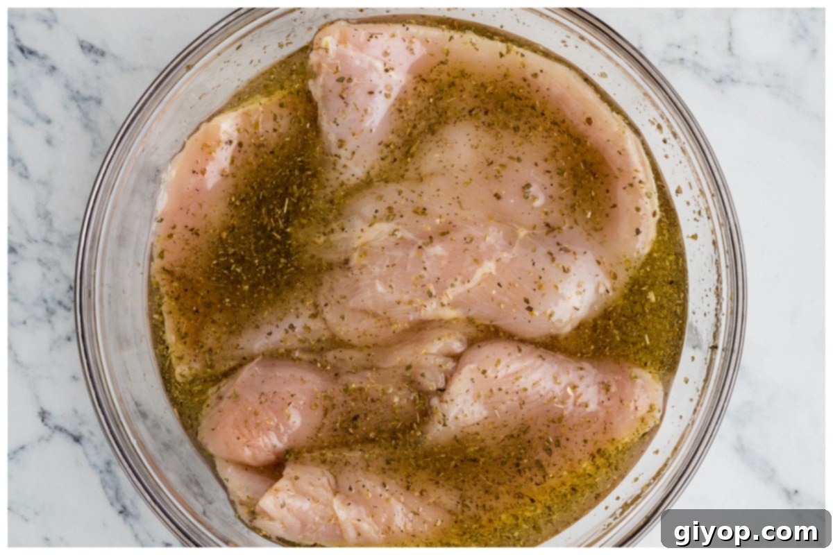 Sun-Kissed Caprese Chicken Sandwich 7 Chicken breasts marinating in a glass bowl, covered.