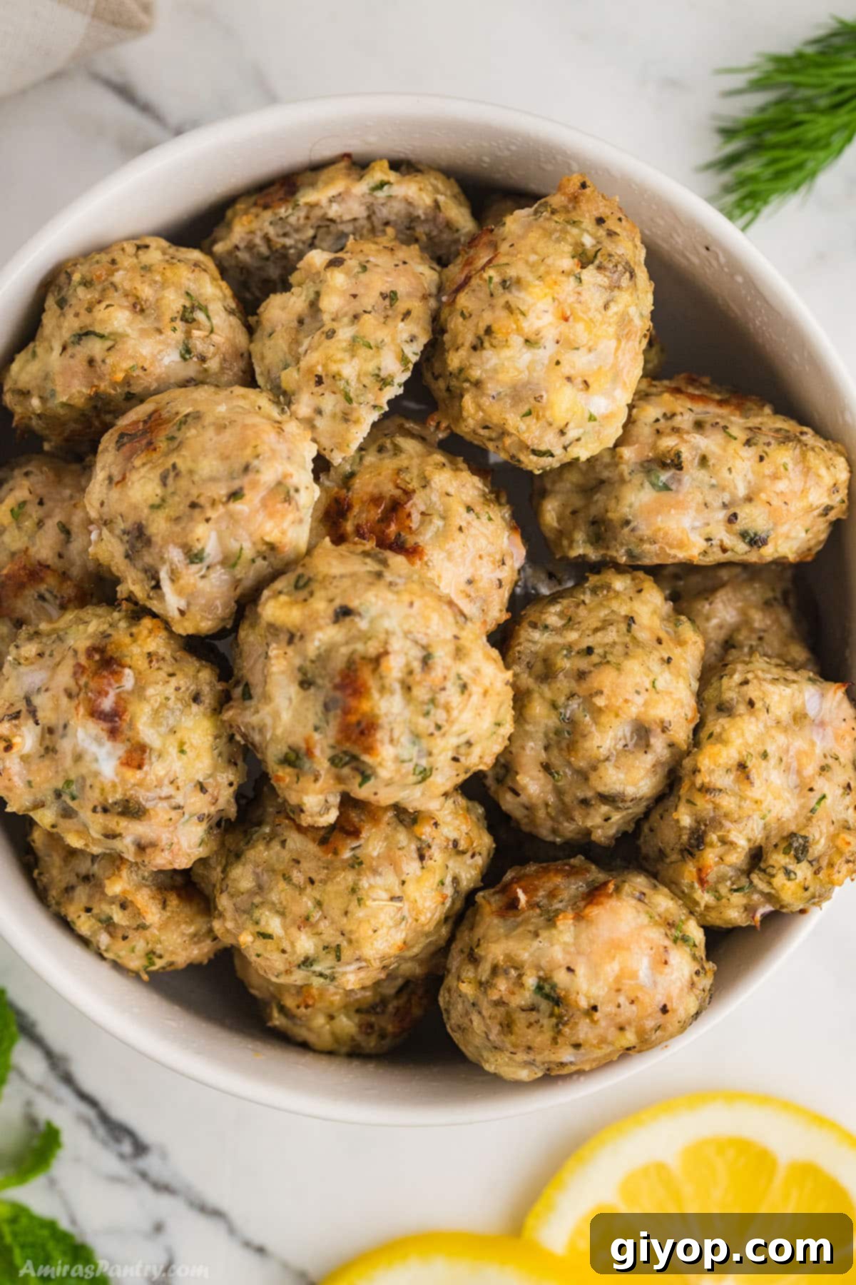 A large bowl filled with golden-brown Greek chicken meatballs, garnished with fresh lemon slices and herbs, ready to be served.
