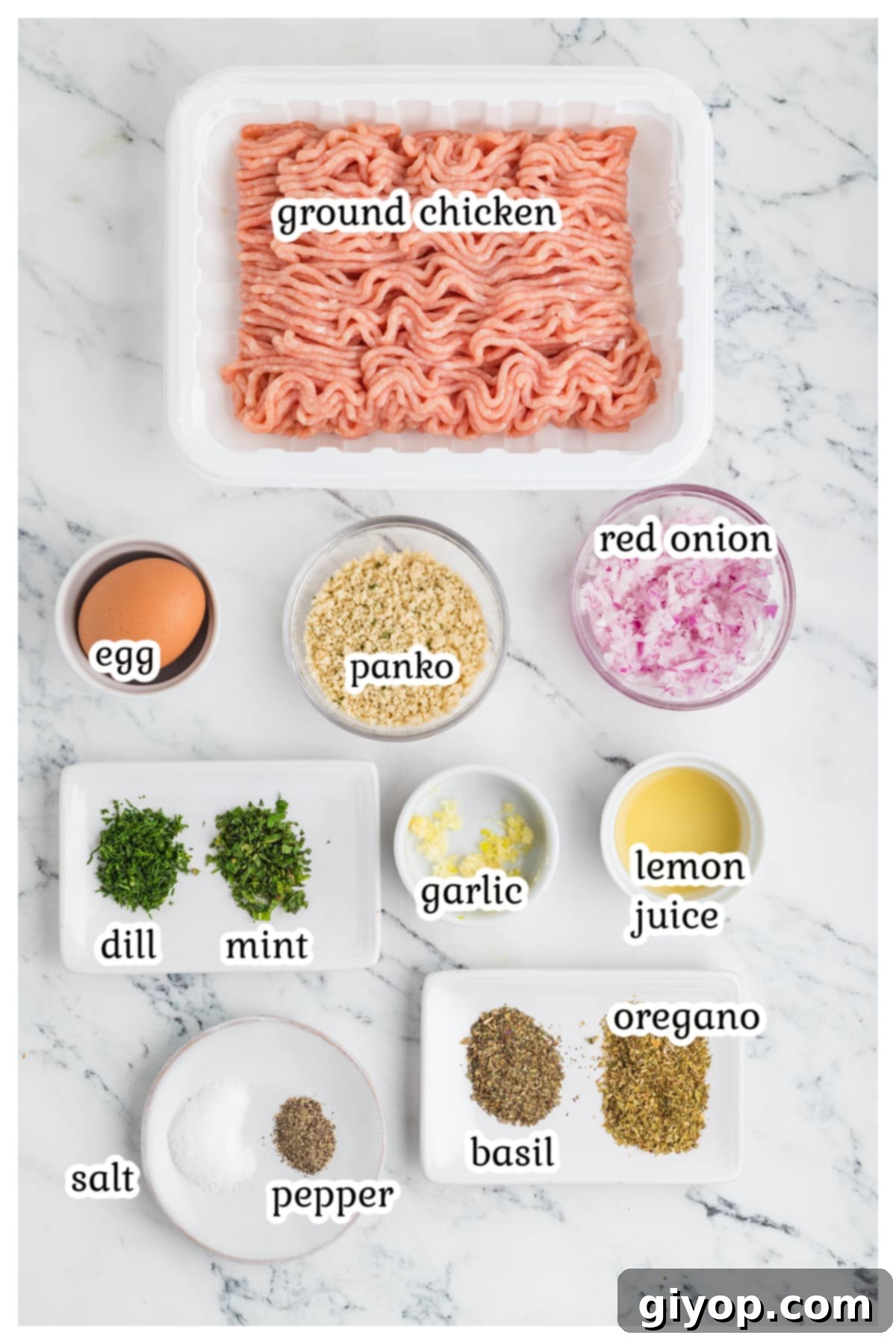 A selection of fresh ingredients for Greek chicken meatballs laid out on a wooden cutting board, including ground chicken, red onion, fresh herbs, lemon, and spices.