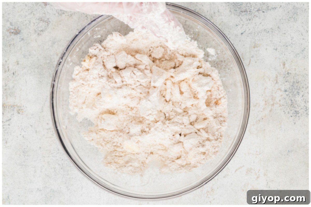 Decadent Salted Caramel Apple Pie Bars 7 A large clear glass bowl filled with a mixture of flour and cold cubed butter, being worked together to form the shortbread crust crumbs.