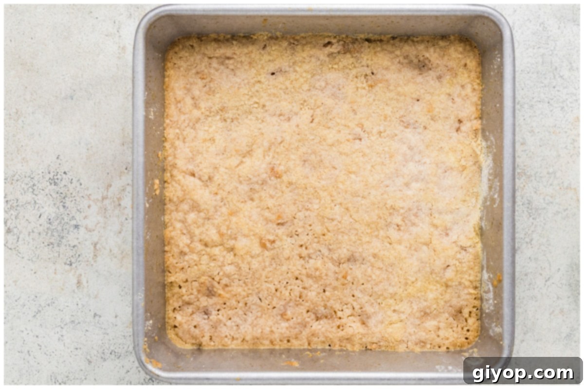 Decadent Salted Caramel Apple Pie Bars 9 A perfectly par-baked shortbread crust, golden-brown at the edges, resting in a light-colored 8x8 inch baking pan, cooling after its initial bake.