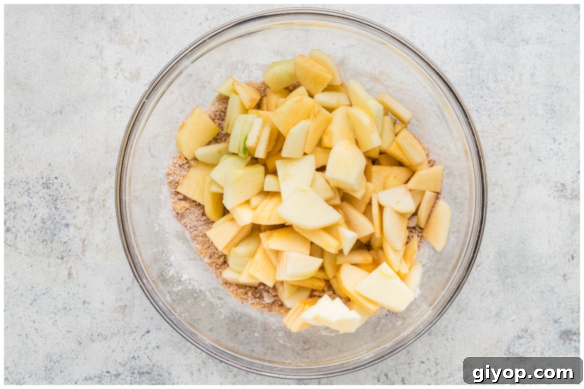 Decadent Salted Caramel Apple Pie Bars 10 Thinly sliced apples mixed with brown sugar, cornstarch, cinnamon, and nutmeg in a large glass bowl, ready to be layered onto the crust.