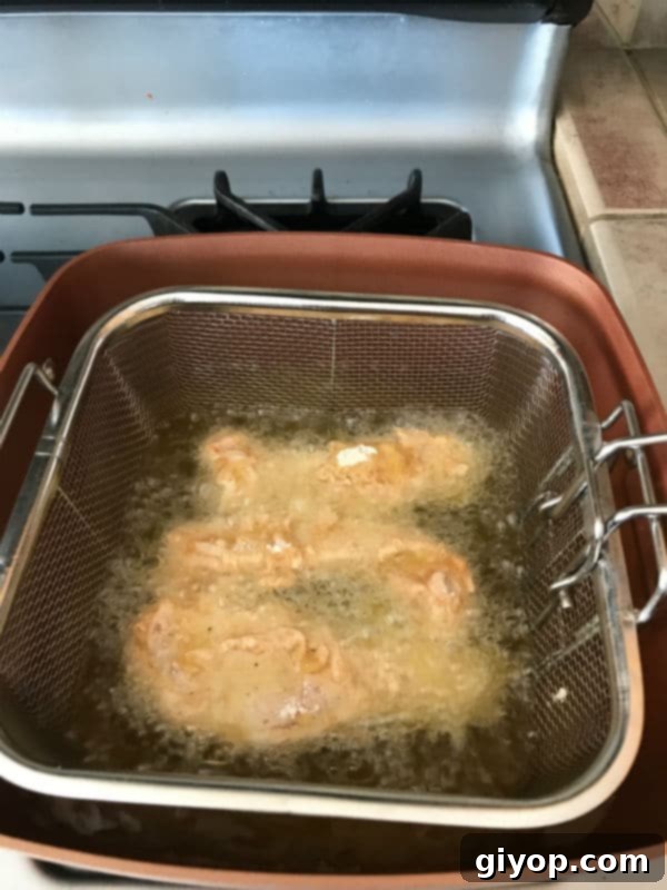 Golden chicken strips frying in hot oil on a stovetop, achieving a perfect crisp.
