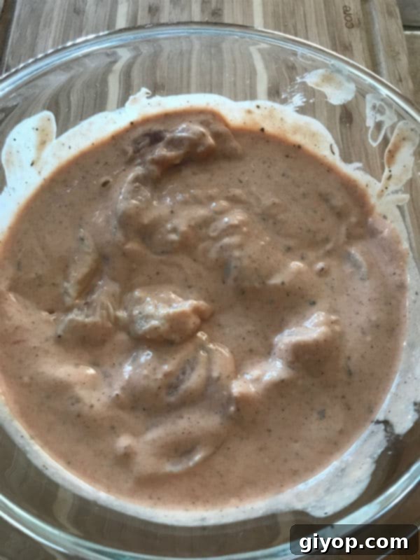 Chicken strips submerged in the flavorful marinade within a glass bowl, ready for chilling.