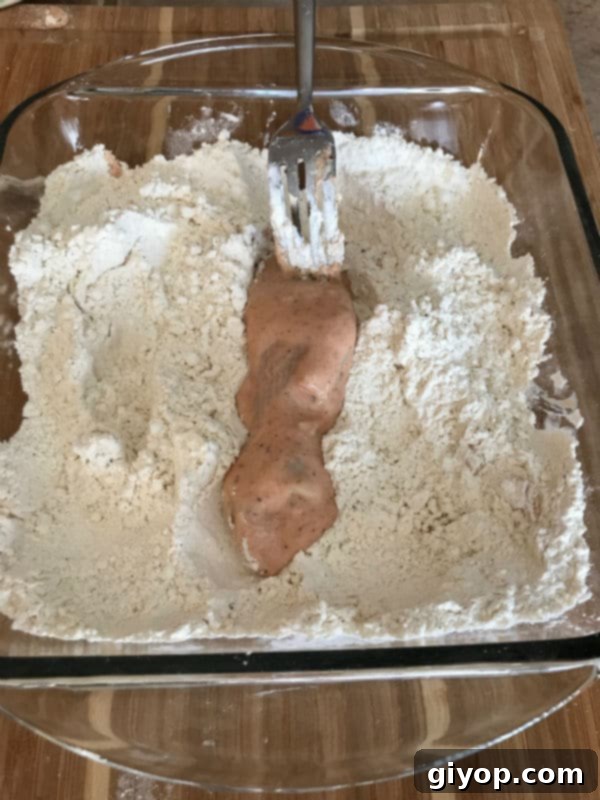 Marinated chicken strip being lightly coated in the dry breading mixture.