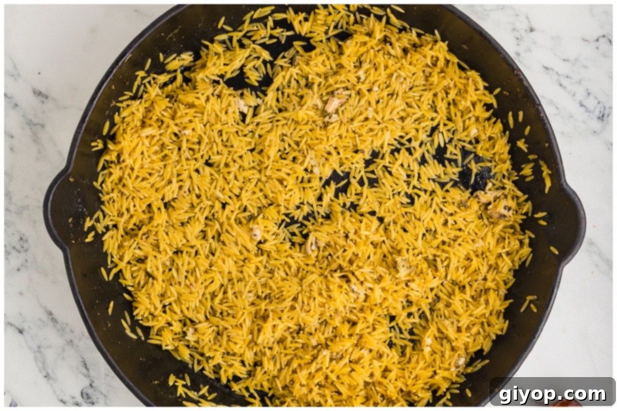 Bright Lemon Chicken Orzo 8 Uncooked orzo pasta being toasted in a large skillet with olive oil, lemon zest, and minced garlic.