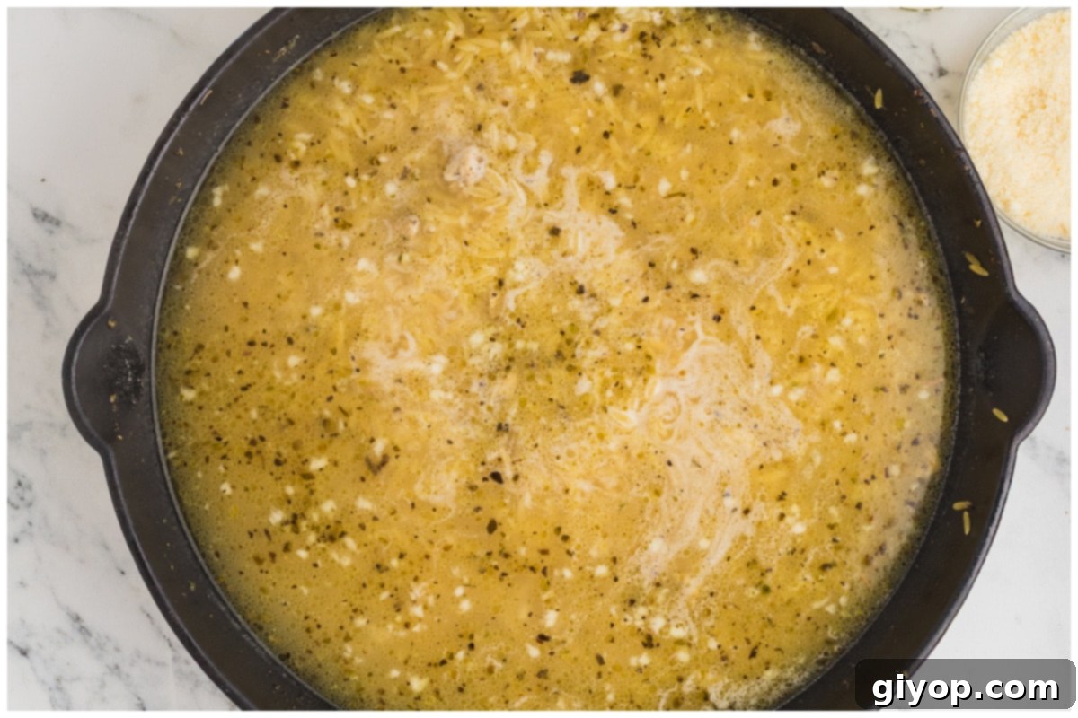 Bright Lemon Chicken Orzo 9 Orzo pasta simmering in a large skillet, covered with chicken broth, absorbing rich flavors.