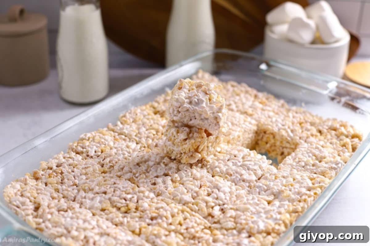 A large baking pan filled with freshly made, golden-brown Rice Krispie treats, with one square carefully removed, showcasing the chewy texture.