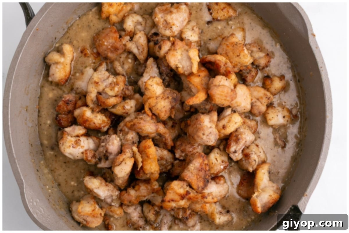 A large skillet filled with perfectly cooked chicken thigh pieces glistening in the rich, thick garlic butter sauce.