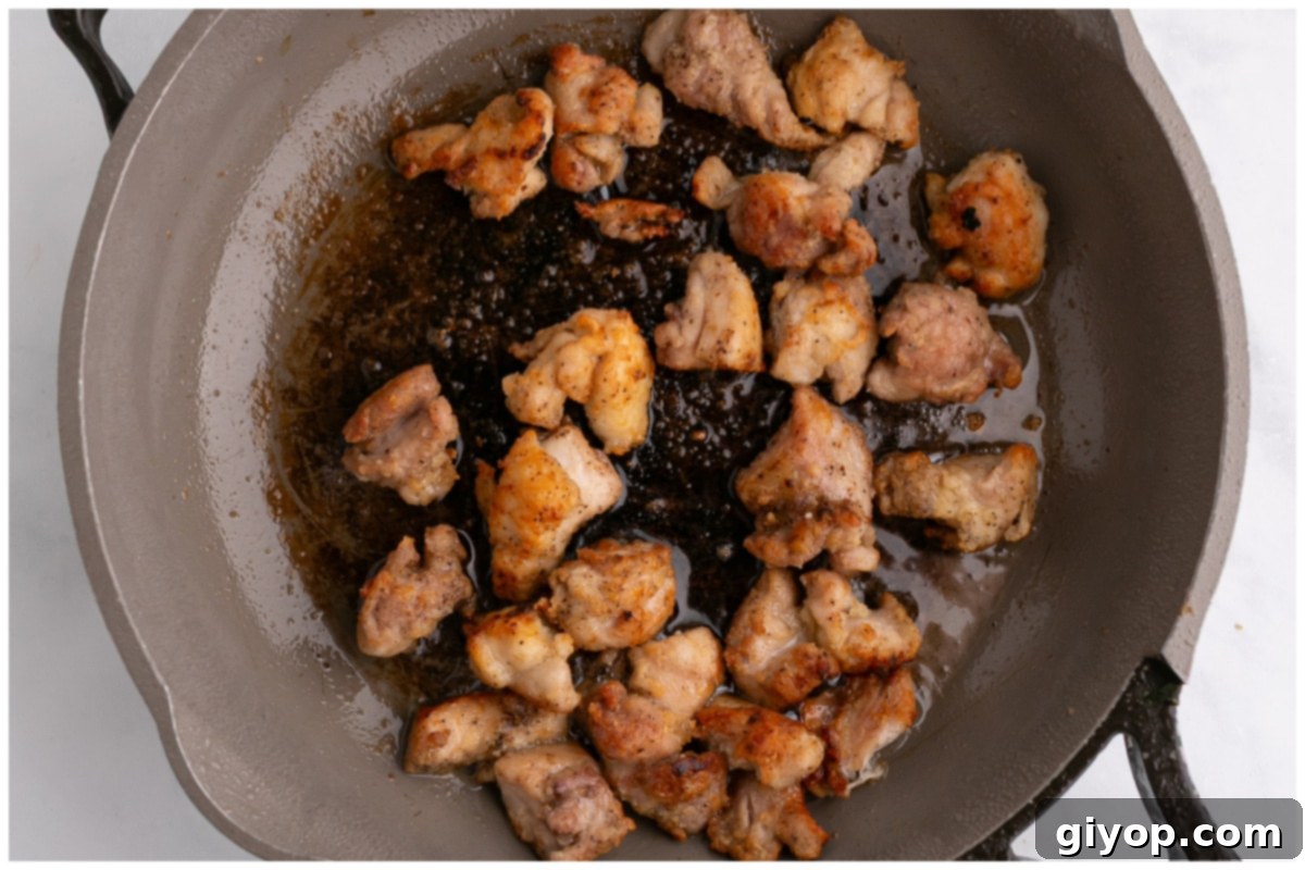 Cubed chicken thighs searing in a large skillet, developing a golden-brown crust.