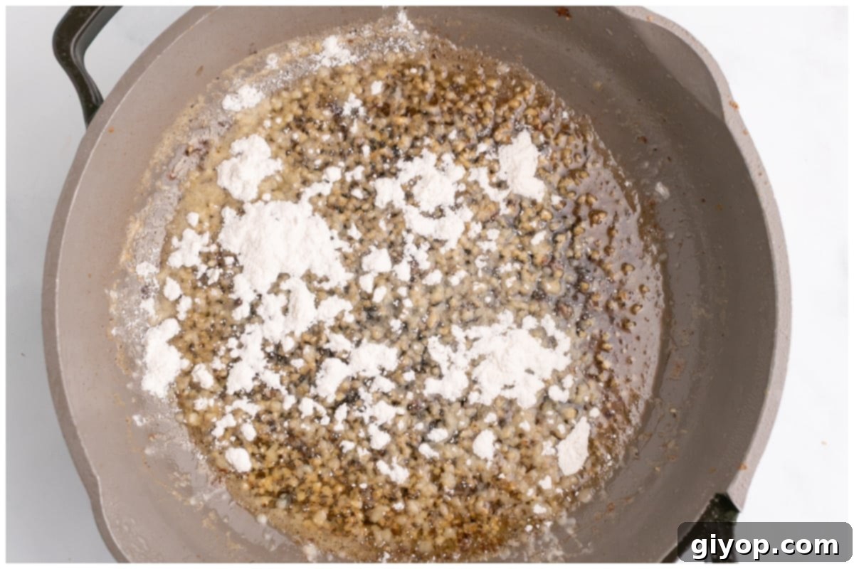 Flour being sprinkled over the garlic butter mixture in a skillet, creating the roux for the sauce.