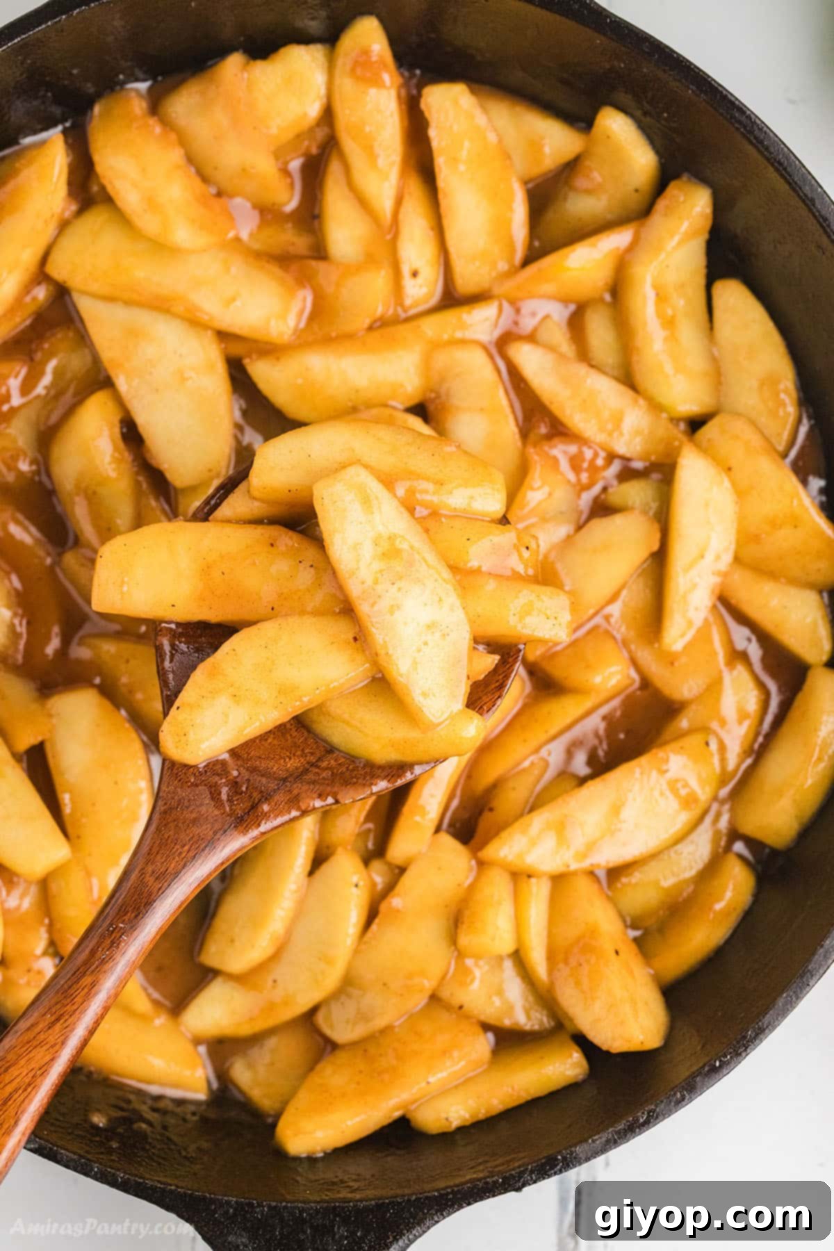 An overhead image of a skillet with golden-brown fried apples, glistening with a buttery cinnamon glaze.