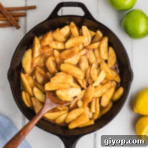 An overhead image of a black skillet with a wooden spoon scooping some fried apples.