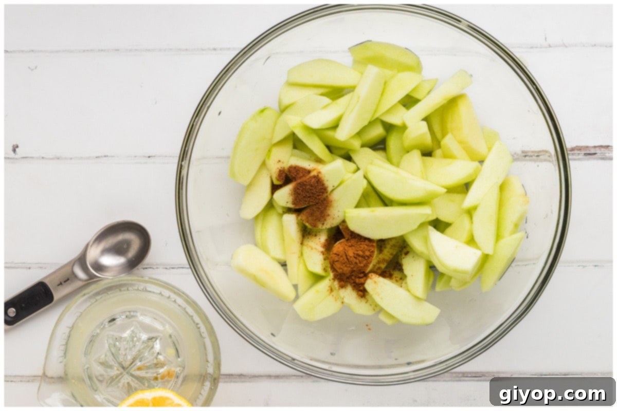 A large glass bowl filled with thinly sliced apples, perfectly seasoned with cinnamon and nutmeg, ready for cooking.