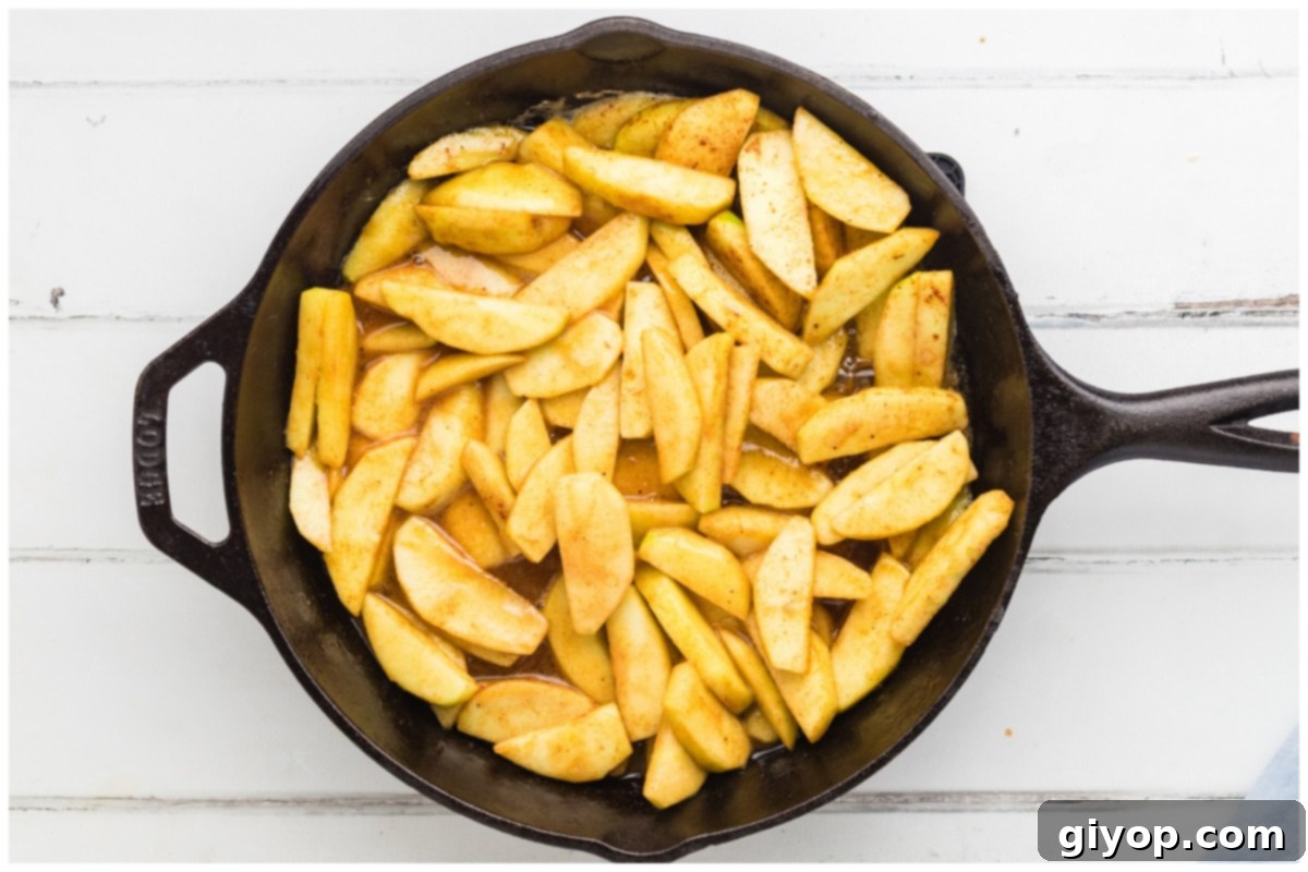 A large skillet filled with cooking apple slices, gently stirring to ensure they are evenly coated in the sweet, spiced glaze.