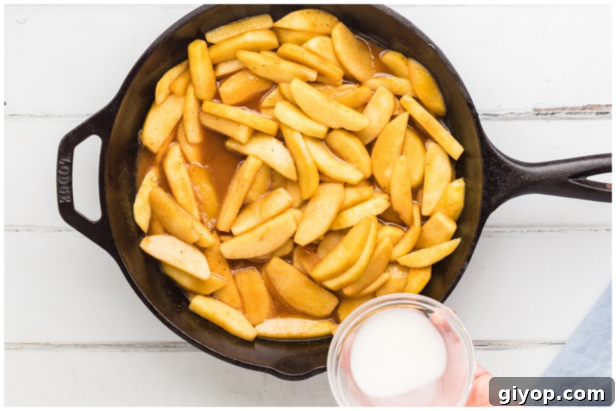 A close-up of a cornstarch slurry being poured into the skillet of cooked apples, ready to thicken the glaze.