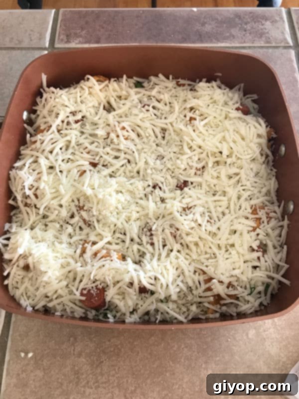 Shredded mozzarella cheese generously sprinkled over the chicken, hot dogs, and rice in the pot, ready for baking.