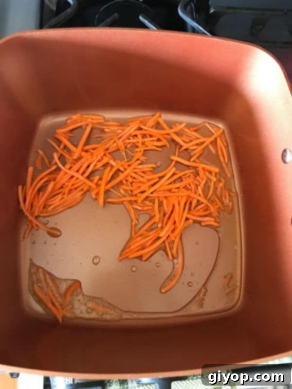 Close-up of shredded carrots sautéing in oil in a pot, turning a dark orange color.