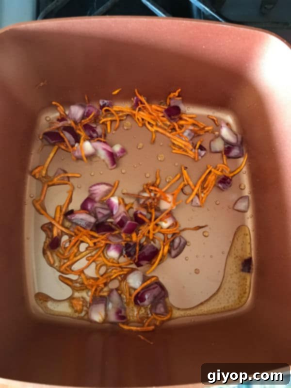 Close-up of diced onions added to sautéed carrots in a pot, cooking until softened.