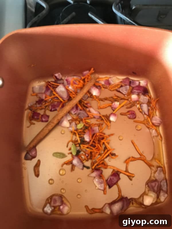 Cinnamon stick, cloves, and cardamom pods added to sautéed vegetables in a pot, releasing their fragrance.