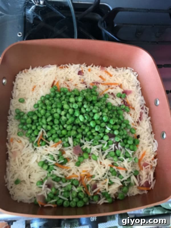Frozen peas added to the partially cooked rice in the pot, continuing to cook.