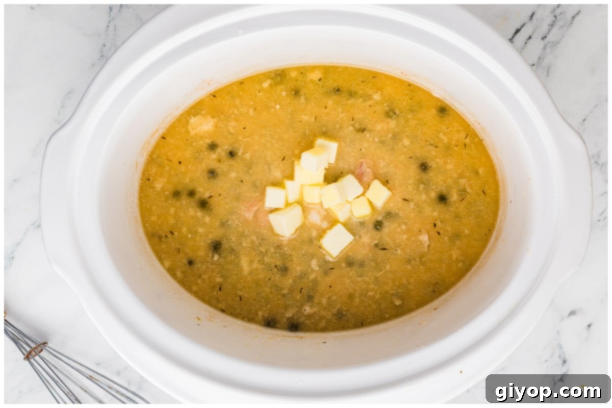 A slow cooker filled with golden chicken piccata, topped with cubed butter melting into the rich lemon-caper sauce.