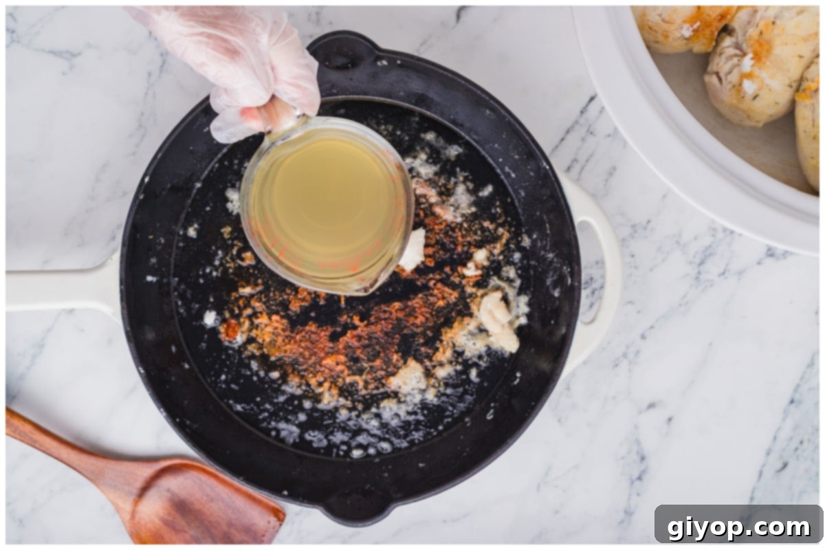 Adding chicken broth to the hot skillet to deglaze the pan and collect all the savory browned bits for the sauce.